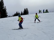 Achtjähriges Kind (im Vordergrund der Guide) mit einer speziellen Übungsform zum Erlernen Gleichgewicht- und Belastungswechsel am Ski