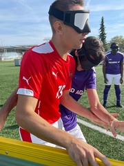 Spieler im roten Shirt hält sich mit einer Hand an der Bande fest und wird von einem anderen Spieler in violetten Shirt bedrängt