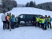 Business-Bus mit Huth-Gastronomie Folie  geparkt vor einer Skipiste. Davor stehen blinde Skifahrer mit ihren Guides