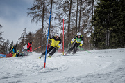 Das Foto zeigt eine dynamische Szene des alpinen Skisports. Zwei Skifahrer (Mike und Tobias Tumfart), die in auffälliger gelb/schwarzer Skibekleidung gekleidet sind, navigieren durch einen Slalomkurs, der mit Stangen markiert ist. Die Atmosphäre verm