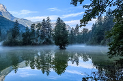 Im Mittelpunkt des Bildes befindet sich der Koppenwinkelsee in Obertraun. Das Wasser ist relativ glatt und reflektiert die umgebende Landschaft, wodurch eine Spiegelung entsteht.