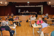 In einem großen Saal sitzen die Spielerinnen und Spieler über ihren Brettern.