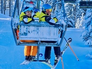 Sehbehinderte Skifahrerin mit Begleitsportlerin am Sessellift bei der letzten Auffahrt in diesem Winter von hinten fotografiert