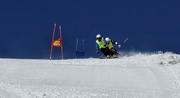 ein Team (Guide und Blindenskiläufer stechen über eine Kante in den Steilhang rein. Im Hintergrund tiefblauer Himmel.